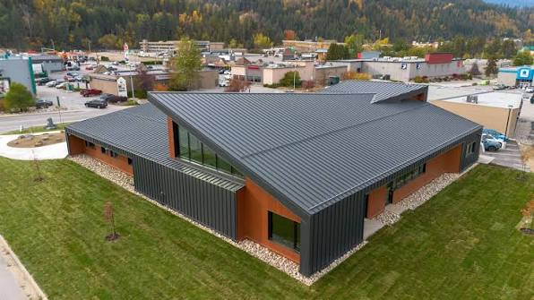 Aerial view of The Confluence building with its multi-angled metal roof, surrounded by grass, the town and forested hills